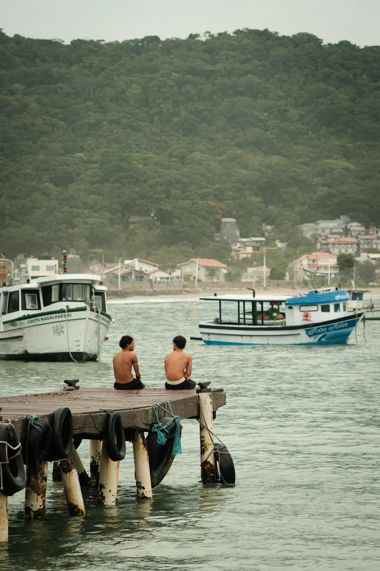 Dois amigos sentados em um píer diante da costa de Florianópolis